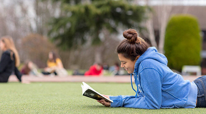 ACS student reading outdoors on a green lawn