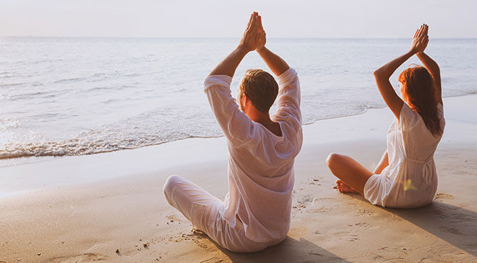 Man and woman do yoga on the beach