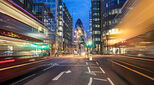 Blurred motion of vehicles moving on street with 30 St Mary Axe in background. Illuminated towers are in city. View of downtown district at night.