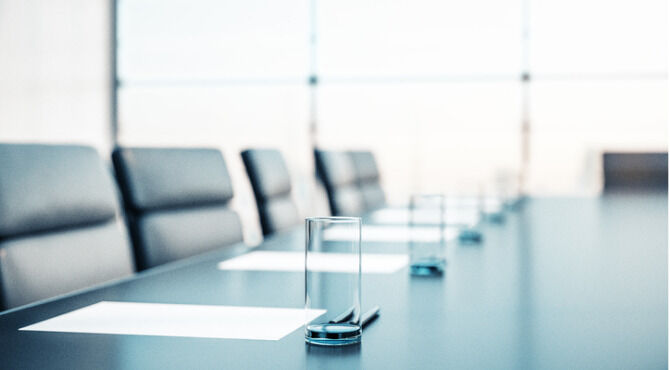 Close up of conference room with glasses of water on the table with papers, armchairs and a large window.