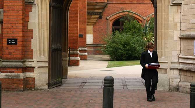 Eton College student pupil walks beneath an archway featuring a statue of Queen Victoria in the Meadow Lane entrance of Eton College, Windsor.