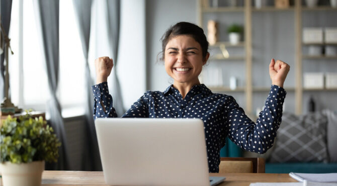 Euphoric young indian girl student winner celebrate victory triumph sit at home desk with laptop computer win online fortune feel excited get new job opportunity good exam result great news concept