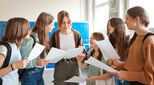 Happy female high school students holding educational exam results, talking and laughing. Teenage girl standing in the school corridor.