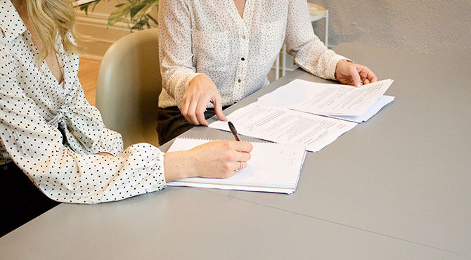 Two women at a work desk, reviewing papers