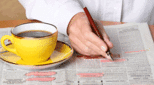 Someone searches for a job in the newspapers while drinking coffee