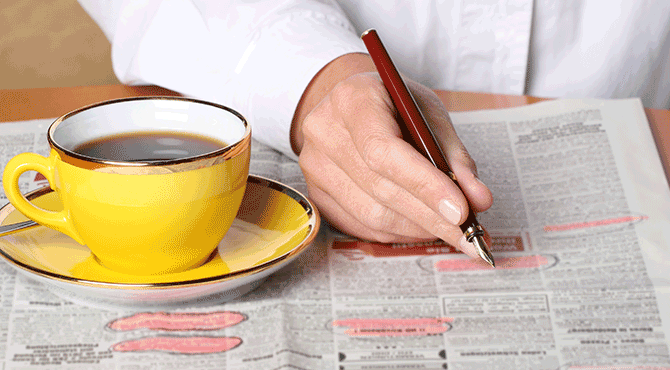 Someone searches for a job in the newspapers while drinking coffee