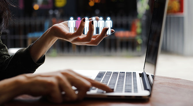 A woman at a laptop holds graphics of people illustrating an article about job vacancies