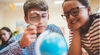 Children in the classroom examining the globe with magnifying glass