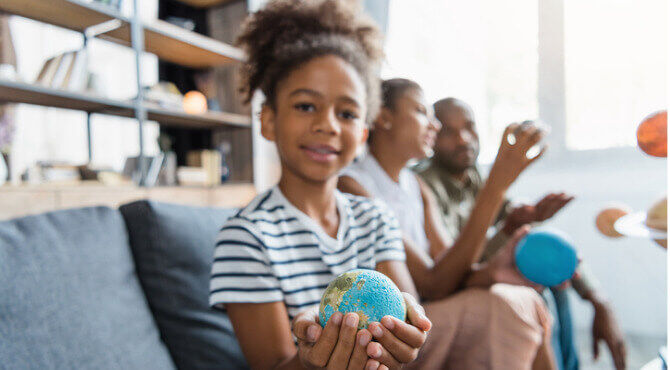 Child holding globe in hands while adults talk in the background