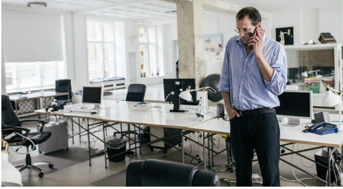 Stressed manager in office amid empty desks on phone