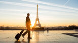 Man with suitcase walks across a piazza with the Eiffel Tower in the background. In Paris