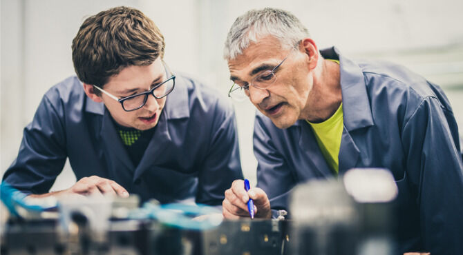 Older engineer and mentee look over work