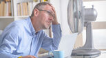 Image of man in office next to fan holding his head