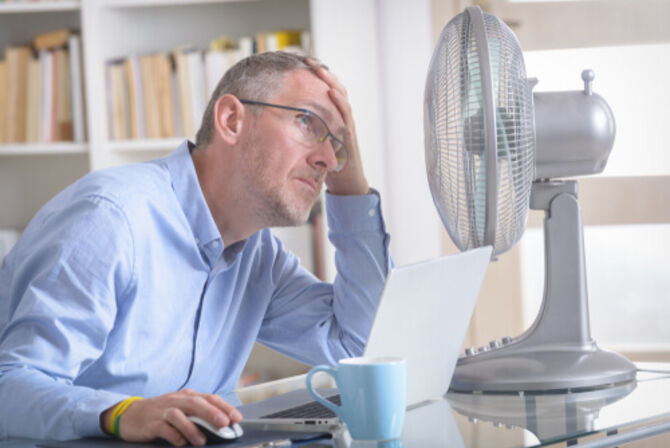 Image of man in office next to fan holding his head