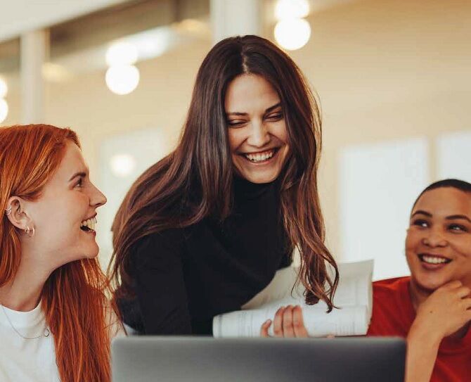 Image of students smiling and chatting by a computer