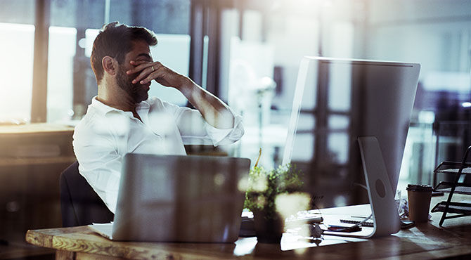 Millennial male in casual work clothes looks stressed out at his computer