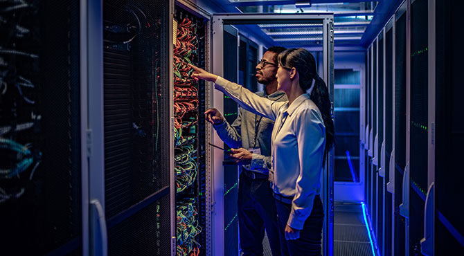 Male and female IT engineers checking servers in server room with help of tablet.