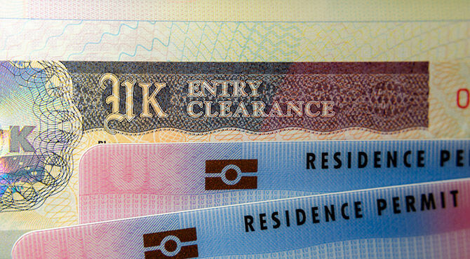 UK BRP (Biometrical Residence Permit) cards for Tier 2 work visa placed on top of UK Entry Clearance vignette sticker in the passport.