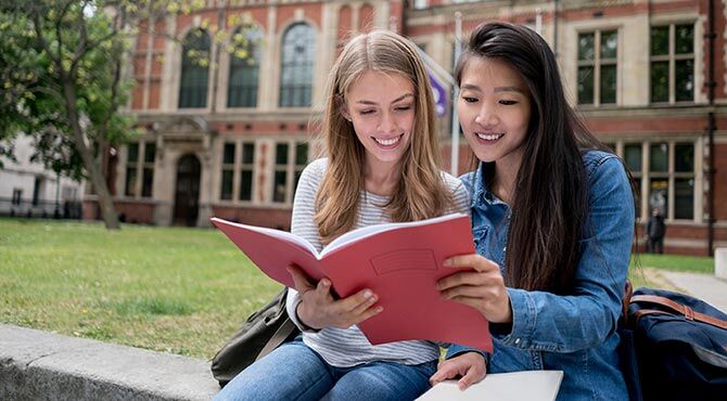 two female students studying outside a brick building