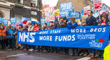 Image of February 2018 NHS crisis march with people and banners supporting migrants and against underfunding