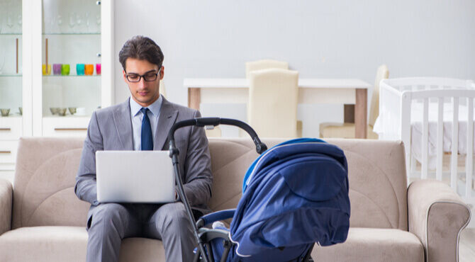Image of man dressed in a suit working on a laptop with a pushchair by his side