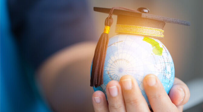 Image of globe in person's hand with mortarboard cap on