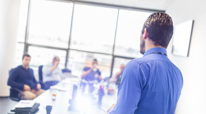 Image of board meeting with rear view of man leading meeting