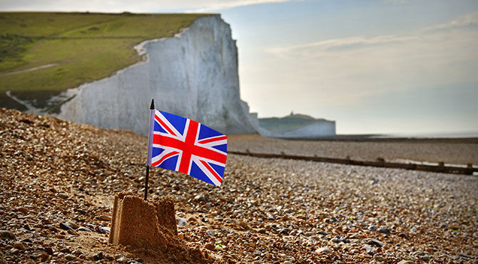 A union jack flag in a sandcastle on a beach with the White Cliffs of Dover in the background