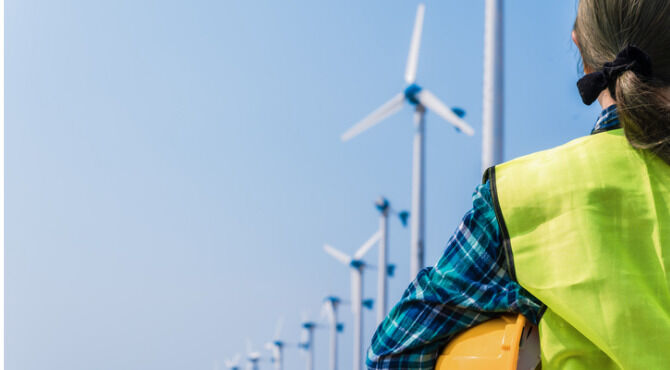 Woman engineer in uniform and holding yellow safety helmet with standing and checking wind turbine power in construction site renewable energy
