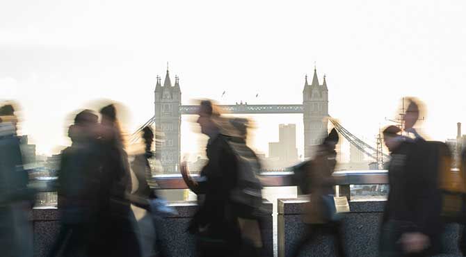 People walk over a bridge with London bridge in the backgroun